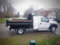 A 2008 Ford F-550 truck with a flatbed and wooden stakes in the back parked on a street