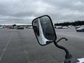 A side mirror of a 2002 Nissan Van reflecting raindrops with a view of a parking lot in the background