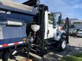 A 2007 International 7300 truck with a white cabin and black chassis, featuring hydraulic controls and a large blue dump body attached to the rear.