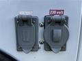 Two gray electrical power outlets mounted on a white surface labeled 115 volt and 230 volt