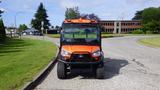 A 2018 Kubota RTV X1100c utility vehicle with an orange body and black accents positioned on a paved surface with tires visible