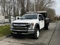 A white 2021 Ford F-550 truck with a flatbed and a black dump body parked on the side of a road