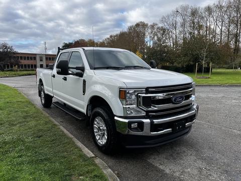 A 2020 Ford F-250 SD in white with a shiny chrome front grille and large wheels is parked on a paved area