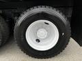 A close-up of a black tire mounted on a white rim with visible bolts and a silver hubcap on a Freightliner truck