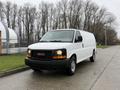 A white 2014 GMC Savana van parked on a paved surface with trees in the background