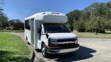 A 2011 Chevrolet Express bus with a white exterior and a high roof parked on a street with its door open