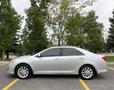A silver 2012 Toyota Camry parked with a side view showcasing its sleek design and alloy wheels