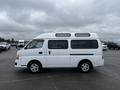 A white 2002 Nissan Van with a high roof and windows on top parked in a lot