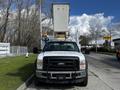 A 2008 Ford F-550 with a large bucket lift attached at the rear parked on a street with trees in the background