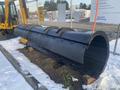 A large black snow plow attachment with a curved blade positioned on a wooden base