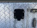 A black electrical connector attachment mounted on a metallic diamond-plate surface