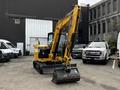 A 2024 Caterpillar 306 compact excavator with a black bucket and yellow body is parked on a paved surface, facing forward