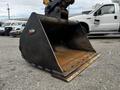 A large metal excavator bucket with a smooth edge and several teeth at the bottom positioned on a flat surface