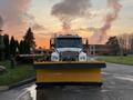 A 2006 Freightliner M2 106 snowplow with a large yellow blade attached at the front positioned on a roadway