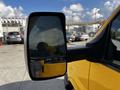 A yellow 2017 GMC Savana with a side mirror reflecting an adjacent vehicle in a parking lot