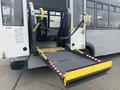 A 2016 Chevrolet Express with a lowered wheelchair ramp supported by yellow safety handles and secured with black straps