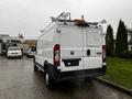 A white 2018 RAM Promaster van with a high roof and ladder racks on top is parked with its rear facing the viewer