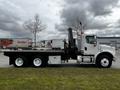 A 2006 Freightliner M2 112 truck with a black flatbed and a hydraulic lift system is parked with six wheels and a white cab