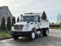 A white 2015 International DuraStar 4300 dump truck with a flatbed and orange warning lights on the roof