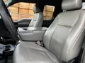 A 2016 Ford F-150 interior featuring two light grey fabric seats with a central console and cup holders between them