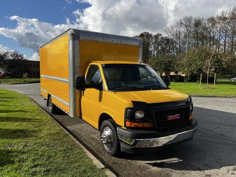 A yellow 2017 GMC Savana truck with a large enclosed cargo area and a chrome front grille parked on the side of a street