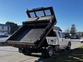 A white 2011 Ford F-350 SD with a dump bed raised revealing the black surface of the bed and rear lights illuminated