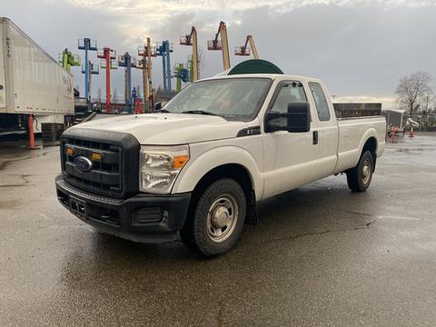 A 2013 Ford F-250 SD in white with a black grille parked on wet ground with a slightly angled front view