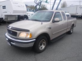 A beige 1998 Ford F-150 pickup truck with a black hood protector and chrome grille parked with a bed liner and two doors