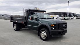 A green 2008 Ford F-450 SD flatbed truck with a dump bed and a prominent front grille parked in a lot