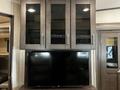 A dark wood entertainment center with a large flat-screen TV below and glass-front cabinets above