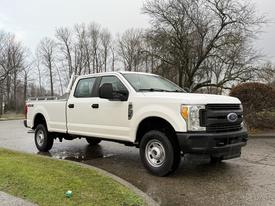 A white 2017 Ford F-350 Super Duty pickup truck with four doors and a bed, parked on a wet surface surrounded by trees