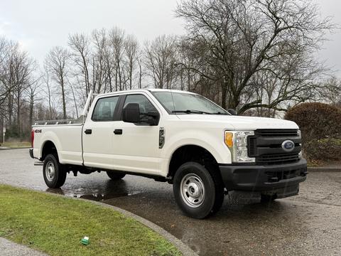 A white 2017 Ford F-350 Super Duty pickup truck with four doors and a bed, parked on a wet surface surrounded by trees