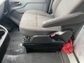 A gray fabric driver's seat in a 2018 Ford Transit with a low-profile storage compartment beneath it and a red item partially visible on the floor