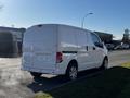 A white 2017 Nissan NV200 van parked on the side of the street with a blank rear license plate and visible exhaust vapor