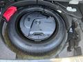 A spare tire with a protective cover and a jack stored in the trunk of a 2023 Mazda MAZDA3