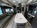 Interior of a 2021 Grand Design Recreational 311BHS featuring a modern kitchen island with a sink and a stovetop along with a comfortable seating area near the window