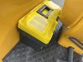 A yellow tool box with a transparent lid placed on a black textured surface next to a piece of machinery