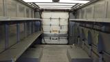 Interior of a 2011 Ford Econoline showing empty metal shelves on both sides and a rear roll-up door