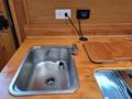 A stainless steel sink with a curved faucet is positioned on a wooden countertop with a cutting board on one side and a charging outlet mounted above it