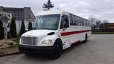 A white 2013 Freightliner M2 106 bus with red accents and multiple windows parked on a paved surface