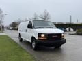 A white 2014 GMC Savana van parked on a street with a flat front and side cargo doors