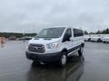 A 2017 Ford Transit van in a white and gray color scheme with sliding side doors and alloy wheels parked on a wet surface