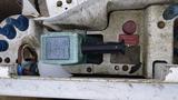 A green hydraulic pump with a black lever on a machinery panel showing various switches and components